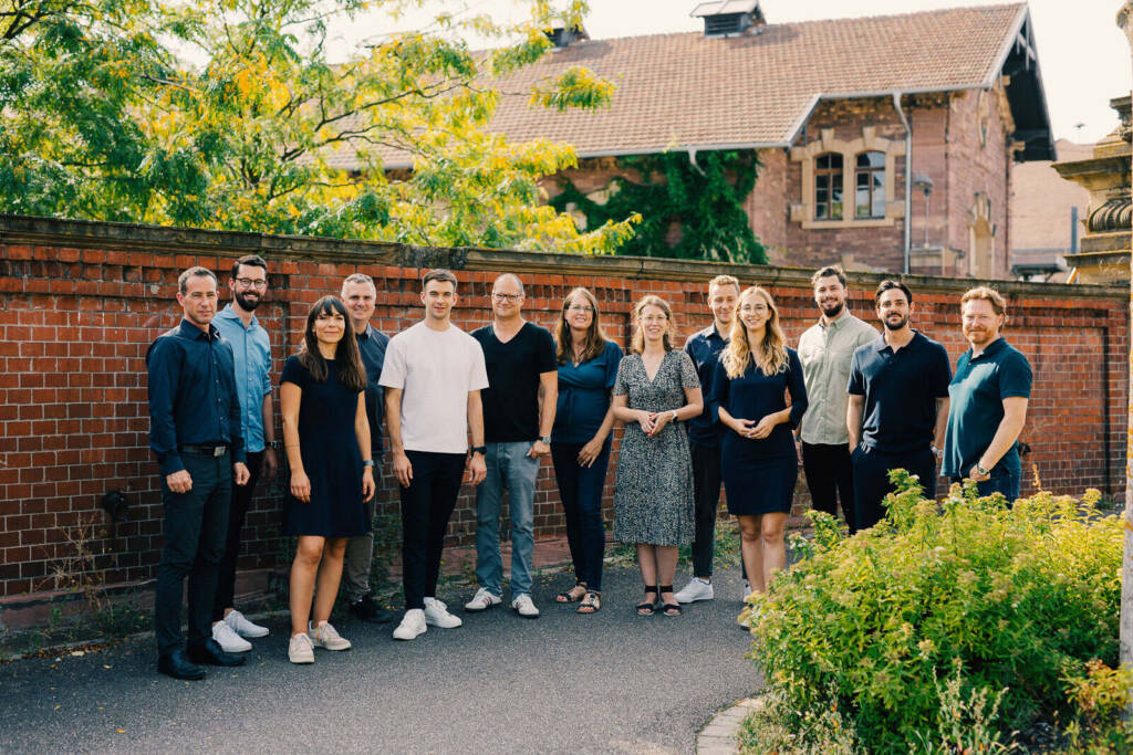 Gruppenporträt eines Teams im Freien vor roter Backsteinmauer – Portraitfotografie zum Thema Portraitfotografie Karlsruhe - Foto von in Team